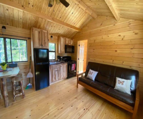 Cozy wooden cabin interior featuring a kitchen, dining area, and a brown sofa with decorative pillows.