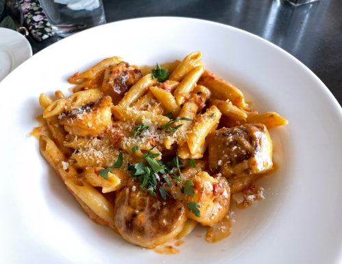 A plate of pasta with shrimp, garnished with parsley and cheese, served in a rich tomato sauce.