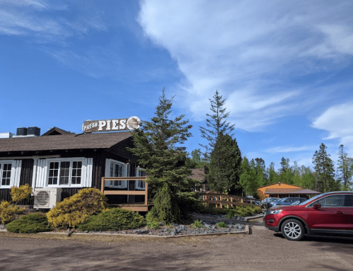 A cozy building with a sign for "Fresh Pies," surrounded by trees and a red car parked nearby under a blue sky.