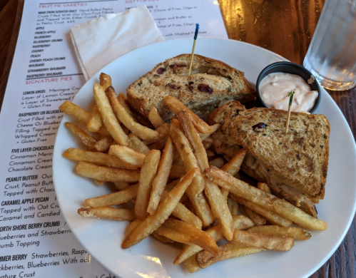 A plate with a sandwich and fries, accompanied by a small cup of dipping sauce. Menu in the background.