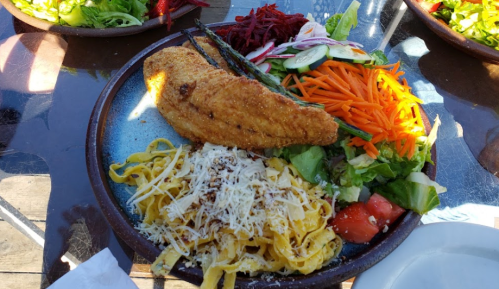 A plate with fried fish, fettuccine pasta topped with cheese, and a fresh salad with various vegetables.