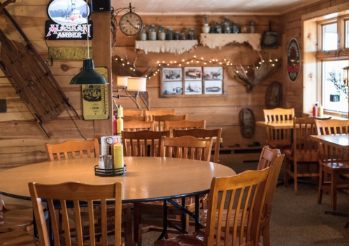 Cozy wooden restaurant interior with round tables, chairs, and rustic decor, including vintage photos and a neon sign.