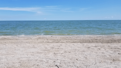 A sandy beach with gentle waves lapping at the shore under a clear blue sky.