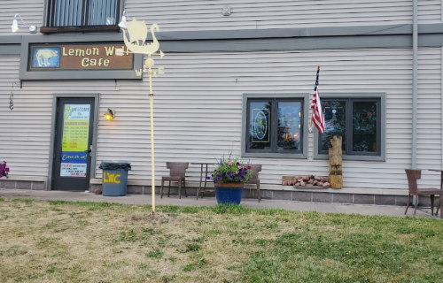 Exterior of Lemon Water Café featuring a sign, windows, an American flag, and outdoor seating with flower pots.