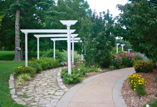 A serene garden path with white trellises, surrounded by colorful flowers and lush greenery.