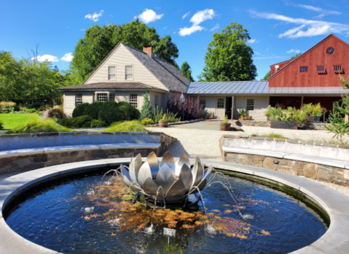 A serene garden scene featuring a lotus fountain, a house, and a red barn under a clear blue sky.