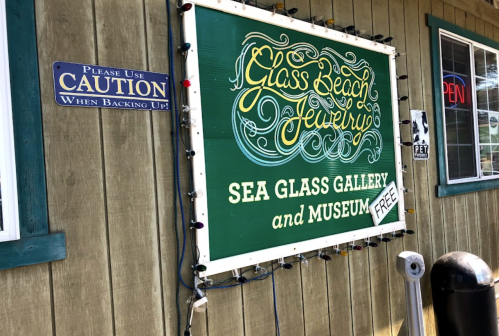 Sign for "Glass Beach Jewelry" featuring "Sea Glass Gallery and Museum" with a caution sign nearby.