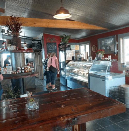 A cozy café interior with a wooden table, a display case, and customers ordering at the counter.