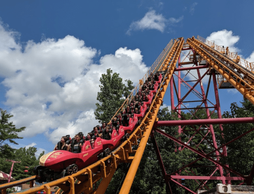 A roller coaster with riders ascending a steep track under a blue sky with fluffy clouds.