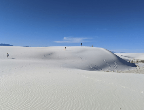 A vast white sand dune under a clear blue sky, with a few people walking in the distance.