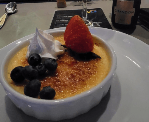 A creamy dessert topped with a strawberry, blueberries, and whipped cream, served in a white dish.