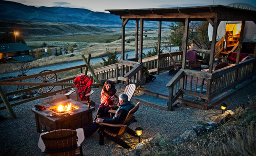 A cozy outdoor seating area with a fire pit, overlooking a scenic landscape at dusk. Two people enjoy the warmth.