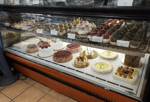 A display case filled with various colorful cakes and pastries, including fruit-topped and cream-filled desserts.