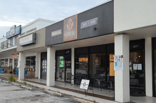 A bake shop with an "Open" sign, featuring outdoor seating and a modern storefront in a shopping area.