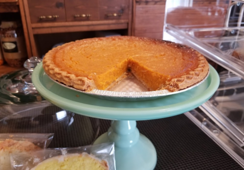A pumpkin pie on a teal cake stand, with a slice cut out, showcasing its smooth filling and golden crust.
