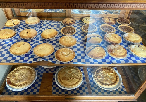 A display case filled with various baked pies on blue checkered paper.