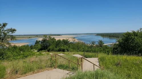 A scenic view of a river winding through green landscapes under a clear blue sky, with steps leading down.