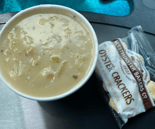 A cup of creamy soup next to a packet of oyster crackers on a table.