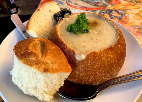 A bowl of creamy soup served in a bread bowl, accompanied by a slice of fresh bread and garnished with parsley.