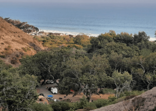 A scenic view of a campsite surrounded by trees, overlooking the ocean and coastline in the distance.
