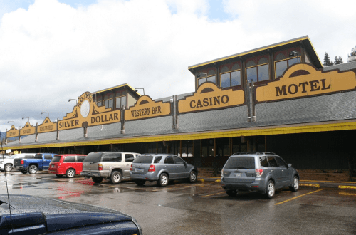 A building with signs for a casino, motel, and bar, featuring a parking lot with several vehicles.
