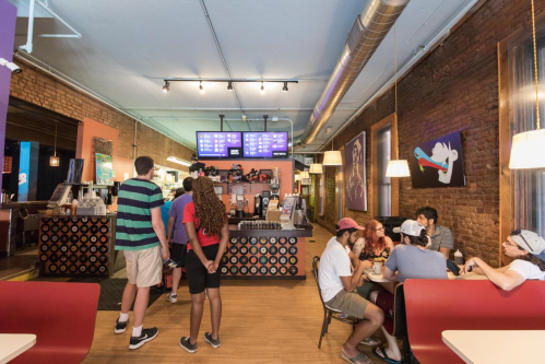 A vibrant café interior with patrons ordering at the counter and others seated at tables, featuring colorful decor.