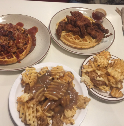 Three plates of food featuring waffles, fried chicken, and waffle fries topped with gravy.