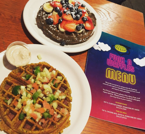 A plate of chocolate waffles topped with fruit and whipped cream, alongside a savory waffle with salsa, and a menu.
