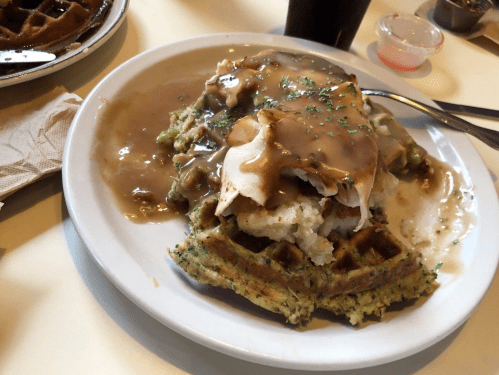 A plate of waffles topped with gravy and a generous serving of turkey, garnished with herbs.