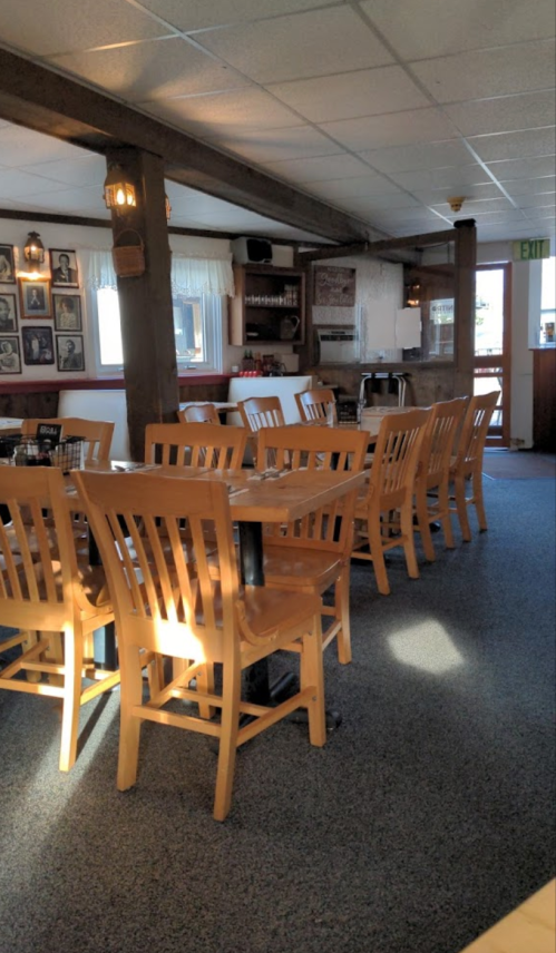 A cozy restaurant interior with wooden chairs, tables, and soft lighting, featuring a carpeted floor and wall decor.