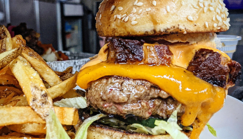 A close-up of a juicy burger with melted cheese, lettuce, and crispy bacon, served with golden fries on the side.