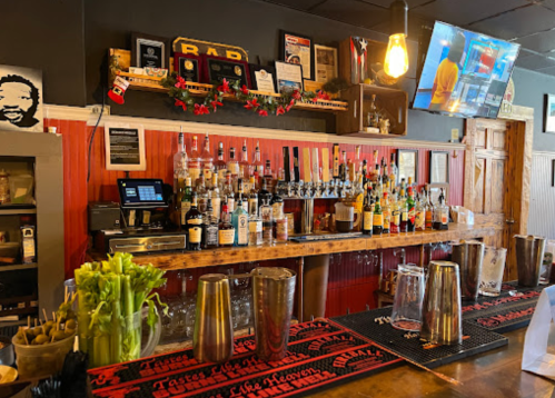 A bar with a variety of liquor bottles, a TV screen, and festive decorations on the wall.