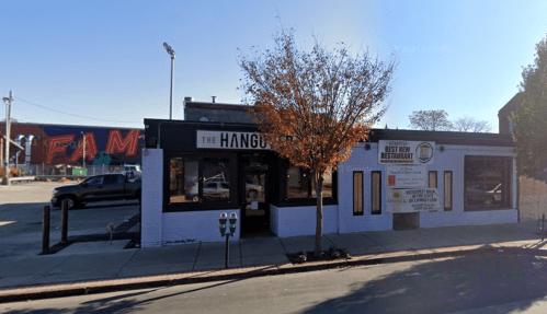 A street view of "The Hangout" restaurant with a tree in front and a colorful mural in the background.