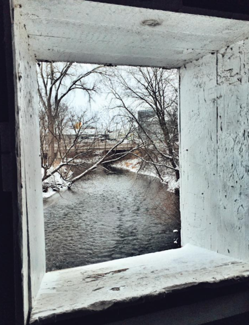 View of a snowy river framed by a wooden window, with bare trees lining the banks.