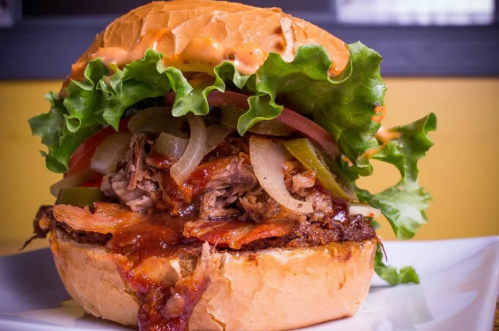 A close-up of a juicy burger with lettuce, tomato, onions, and sauce, served on a toasted bun.