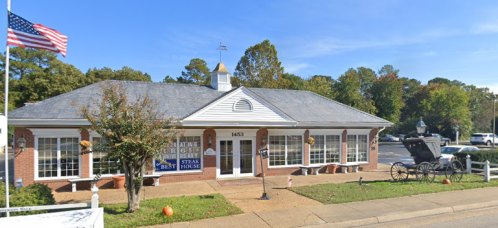 A brick building with large windows, featuring a sign for a steakhouse, surrounded by trees and a horse-drawn carriage.