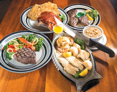 A variety of dishes on plates, including grilled steak, chicken, seafood, and sides of vegetables and sauce.