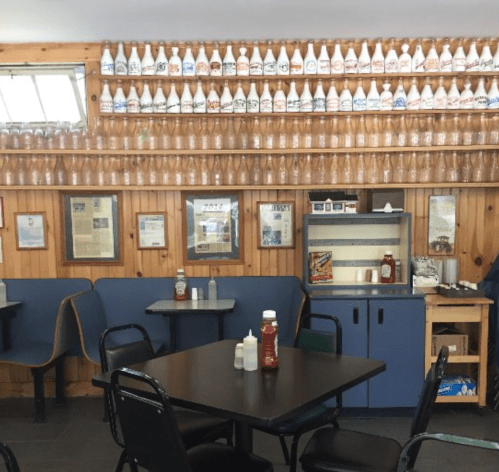 A cozy diner interior with wooden walls, tables, and shelves lined with various bottles and condiments.