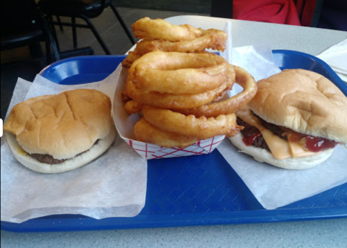 A blue tray with two sandwiches and a basket of onion rings. One sandwich has cheese and ketchup, the other is plain.