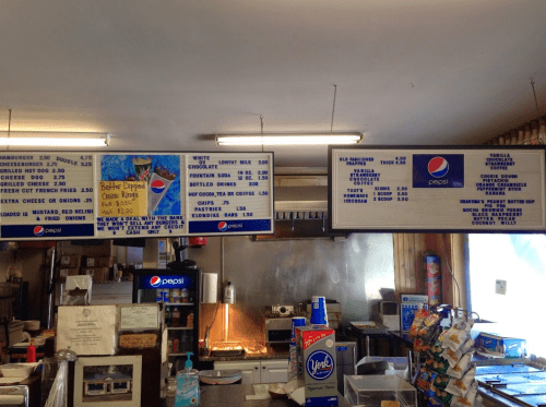 Menu board displaying food and drink options, including burgers, fries, and various beverages, in a casual dining setting.
