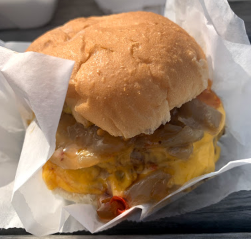 A close-up of a cheeseburger with melted cheese and sautéed onions, wrapped in white paper.