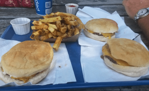 Three burgers with melted cheese and a side of golden fries on a blue tray, with condiments in small cups.