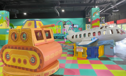 Colorful indoor play area featuring a toy tank and a toy airplane among vibrant flooring and decorations.