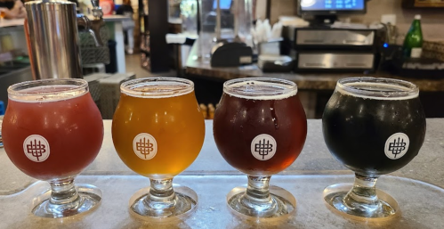 Four small glasses of beer in varying colors—red, gold, amber, and dark brown—on a bar counter.