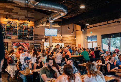 A busy restaurant filled with people dining, chatting, and watching a TV, featuring a warm, inviting atmosphere.