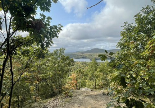 A scenic view of a lake surrounded by trees and mountains under a partly cloudy sky.