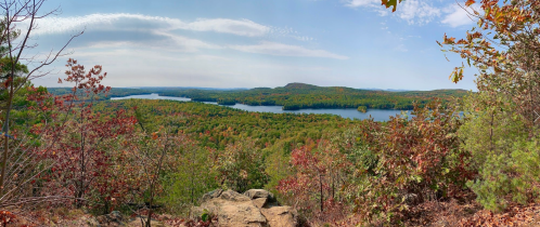Panoramic view of a vibrant autumn landscape with a lake surrounded by colorful trees and a clear blue sky.