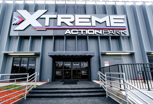 Entrance of Xtreme Action Park with a large sign and modern architecture. Steps lead up to the doors.