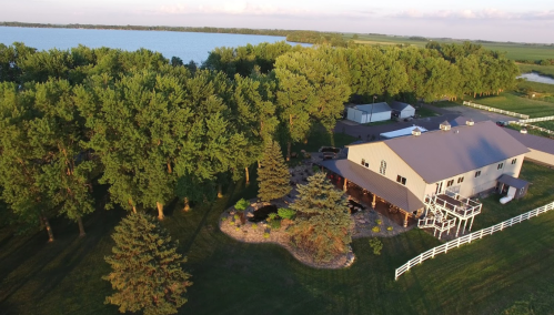 Aerial view of a large house surrounded by trees and a lake, with a landscaped yard and white fence.