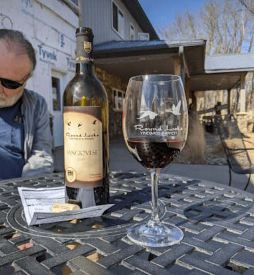 A bottle of Sangiovese wine and a glass on a table, with a person sitting in the background at a winery.